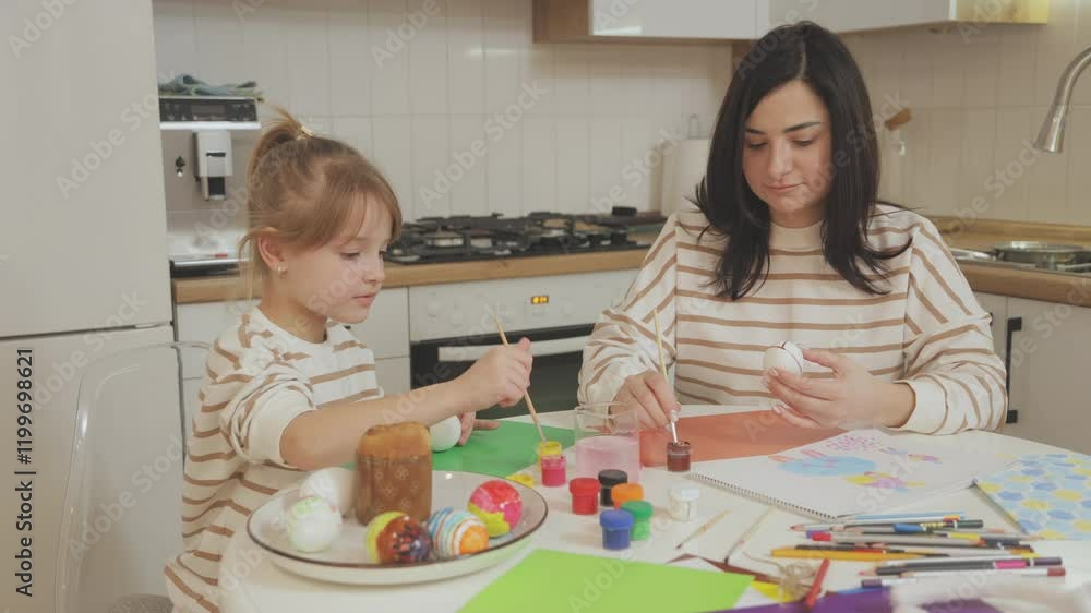 Young beautiful mother and charming daughter are painting Easter eggs. Mom and daughter are getting ready to celebrate Easter. Celebrating Easter with family. Young beautiful mother and charming daughter are painting Easter eggs. Mom and daughter are getting ready to celebrate Easter. Celebrating Easter with family.
