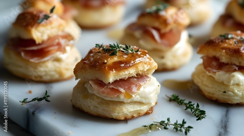 A closeup of snackable Asiago cheese biscuits filled with delicate prosciutto, arranged on a marble platter with a drizzle of honey and scattered fresh thyme leaves photo