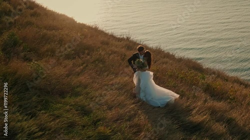 Wedding couple on sunset background. Beautiful bride and groom near the ocean. Honeymoon romantic couple in love holding hands walking in nature. Lovers or newlywed married young couple by the sea.