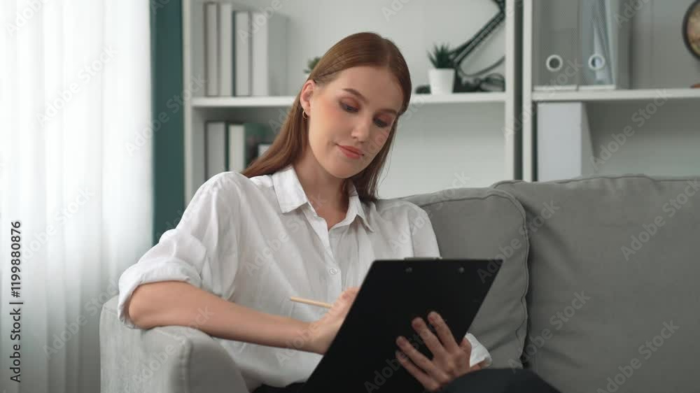 Professional female psychologist with clipboard portrait sitting on arm chair in psychiatrist office or therapy room. Friendly and prim mental healthcare counselor and therapist. Professional female psychologist with clipboard portrait sitting on arm chair in psychiatrist office or therapy room. Friendly and prim mental healthcare counselor and therapist.