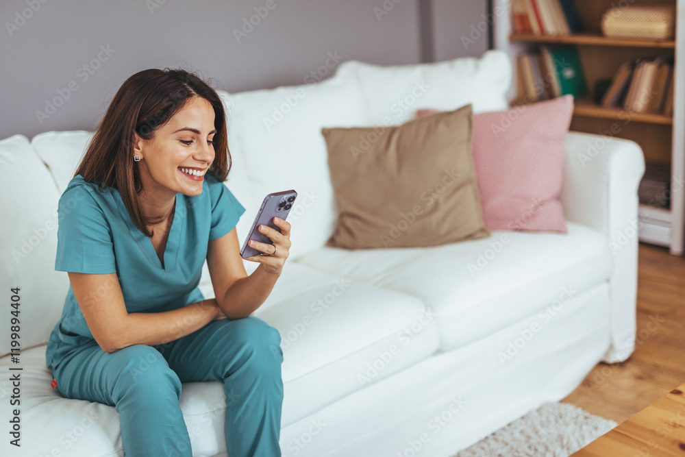 Smiling Woman in Scrubs Using Smartphone on Comfortable White Sofa Smiling Woman in Scrubs Using Smartphone on Comfortable White Sofa