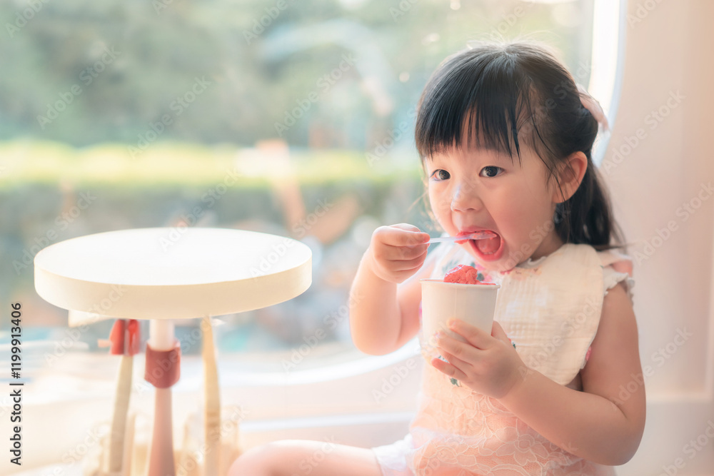Young Asian Girl Enjoying Delicious Ice Cream Treat in Bright Sunny Indoor Setting Young Asian Girl Enjoying Delicious Ice Cream Treat in Bright Sunny Indoor Setting
