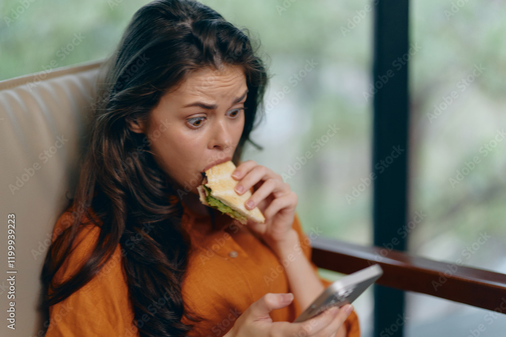 Surprised young woman enjoying a sandwich while texting on her phone, indoors with a stylish background, emphasizing healthy eating and modern lifestyle Surprised young woman enjoying a sandwich while texting on her phone, indoors with a stylish background, emphasizing healthy eating and modern lifestyle