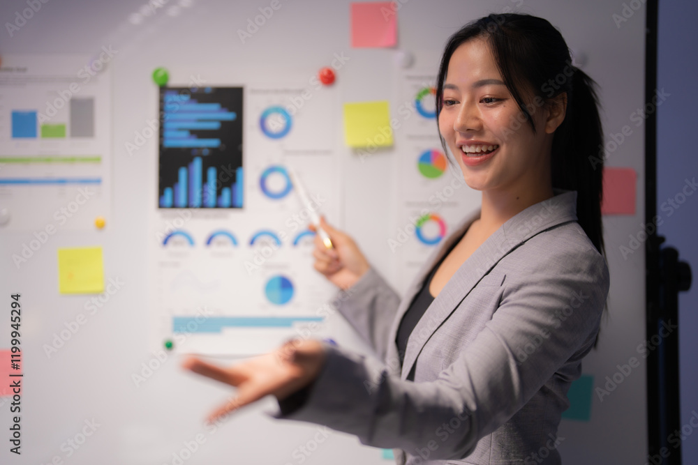 Young professional woman engaging in a business meeting, explaining company strategy while pointing at charts and smiling, showcasing confidence and leadership in the corporate environment Young professional woman engaging in a business meeting, explaining company strategy while pointing at charts and smiling, showcasing confidence and leadership in the corporate environment