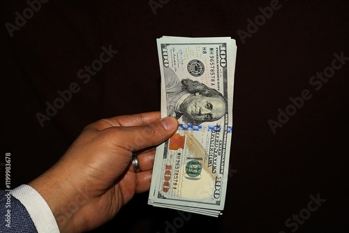 Hand holding a stack of $100 U.S. bills, showing the front side of the notes. stack is isolated on black background, highlighting the details of Benjamin Franklin's portrait and the intricate design