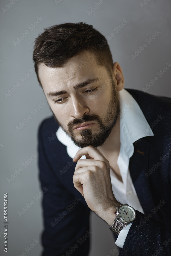 Serious young professional man wearing a formal suit, resting his chin on his hand in a contemplative pose. Perfect for business, corporate, and leadership-themed photography. Serious young professional man wearing a formal suit, resting his chin on his hand in a contemplative pose. Perfect for business, corporate, and leadership-themed photography.