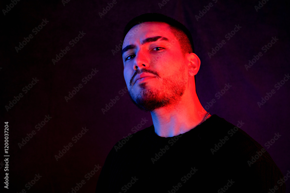 Stylish portrait of a defiant man in moody red and blue lighting, wearing black attire against a dark background Stylish portrait of a defiant man in moody red and blue lighting, wearing black attire against a dark background