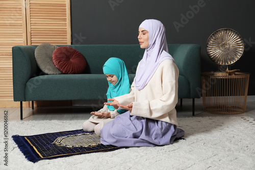 Muslim woman and her daughter praying on mat at home photo