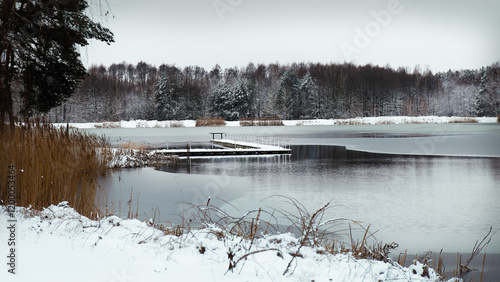 Winter lake landscape with snowy pier. Zelów, Poland, Europe.