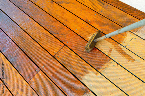Close-up of a wooden deck being stained with a brush for protection and maintenance during a home improvement project in bright sunlight