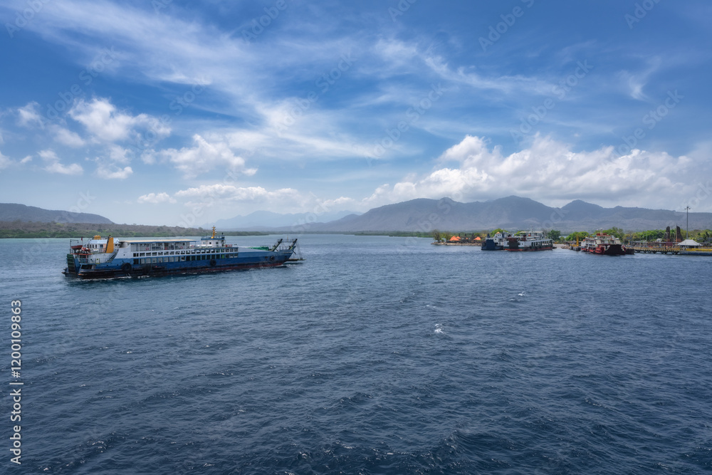 A serene and tranquil harbor is beautifully showcasing various boats floating gracefully on calm waters, all surrounded by majestic mountains under a bright blue sky, Bali, East Java, Indonesia