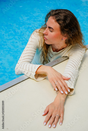 Confident woman with long hair down in a white blouse elegantly posing on the steps of the pool. Slim sexy woman near the pool. photo