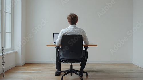 back view of full body of a young man wearing a white shirt and black trousers sitting in an office chair and writing on a desktop apple leptop on a wood office desk on empty white background photo