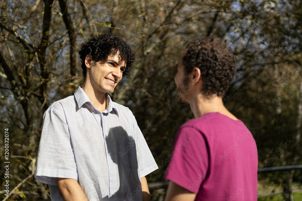 A gay couple looks at each other tenderly while holding hands, showing their love in a sunny park