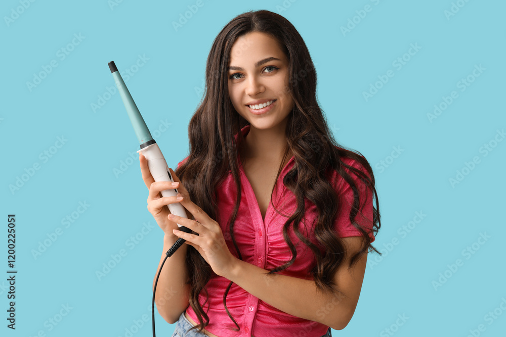 Beautiful young woman with curling iron on blue background Beautiful young woman with curling iron on blue background
