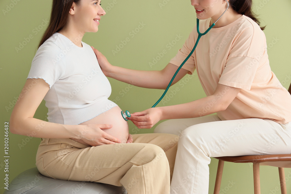 Fototapeta premium Doula listening to pregnant woman's belly near green wall