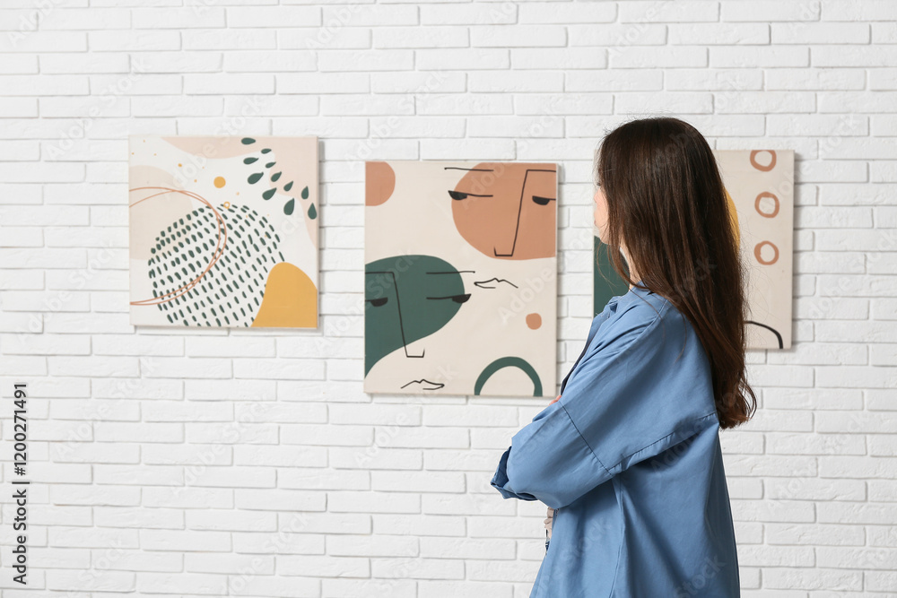 Young woman looking at paintings on white brick wall in art gallery Young woman looking at paintings on white brick wall in art gallery