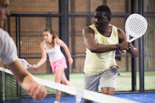 Confident African American man playing padel tennis on indoor court, ready to hit two handed backhand . photo