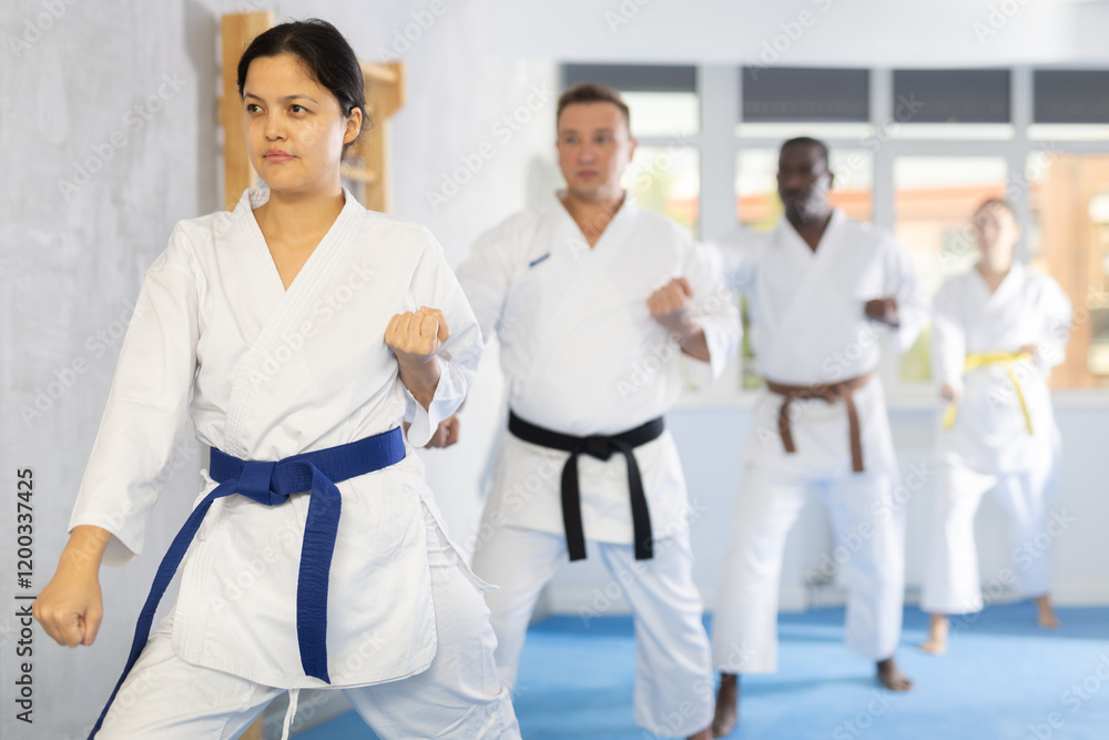 Diligent middle-aged woman attendee of karate classes practicing kata standing in row with others in sports hall Diligent middle-aged woman attendee of karate classes practicing kata standing in row with others in sports hall