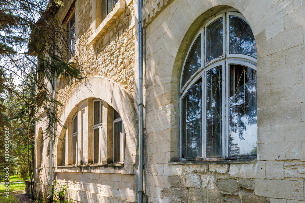 Fototapeta premium Historic stone building with arched windows surrounded by trees in sunlit setting