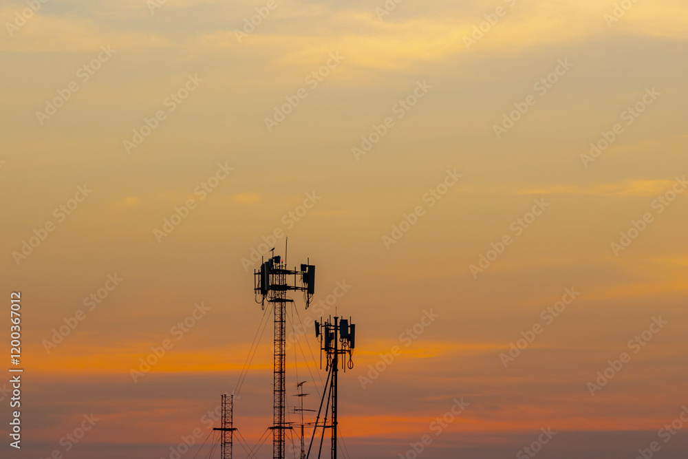 Silhouette of analog TV antenna mast pole on rooftop of high building, Telephone signal tower, Radio engineering used with a transmitter or receiver signal, Golden yellow orange sky sunset background. Silhouette of analog TV antenna mast pole on rooftop of high building, Telephone signal tower, Radio engineering used with a transmitter or receiver signal, Golden yellow orange sky sunset background.