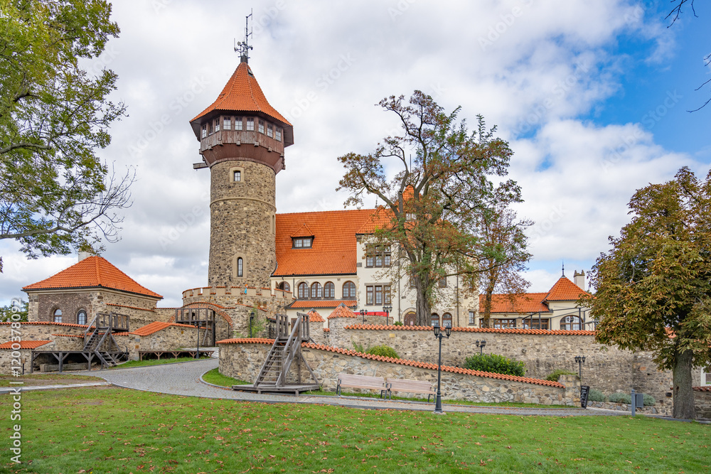 Fototapeta premium Hnevin Castle stands majestically in Most, Czechia, showcasing its stunning architecture against a backdrop of trees and clouds. Visitors can explore the surrounding grounds and enjoy the serene park.