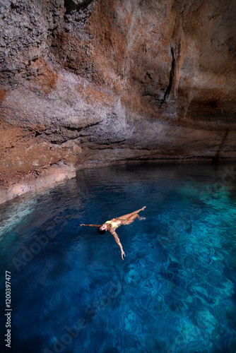 Mujer joven, atractiva, latina en bikini, flotando/nadando en un cenote cristalino, azul turquesa, cerca de Tulum México