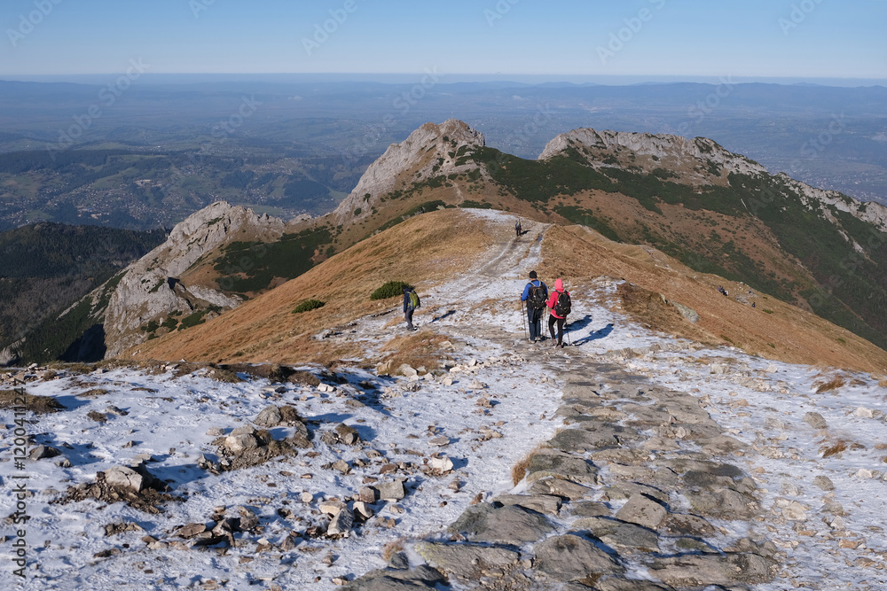 Scenery of autumn Tatras Mountains with silhouettes of hiking people. Giewont Peak on background. Czerwone Wierchy range from around Kasprowy Wierch Peak, Tatras Mountains, Poland.