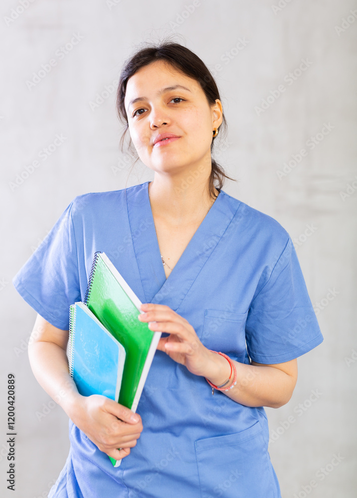 Positive confident young woman, professional doctor, in blue uniform holding medical records. Studio photoshoot on gray background Positive confident young woman, professional doctor, in blue uniform holding medical records. Studio photoshoot on gray background