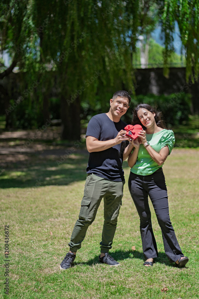 Latin couple in love with a heart-shaped gift in their hands in a park on a bright day Latin couple in love with a heart-shaped gift in their hands in a park on a bright day