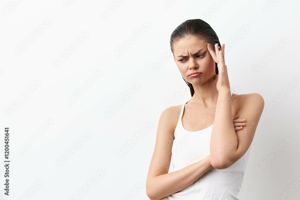 Young woman expressing frustration, touching her head while standing against a plain white background Her body language conveys discomfort and concern, suitable for emotional or mental health themes