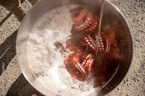 Chef (pulpeiro) preparing fresh octopus by submerging it in boiling water in a large metal pot photo