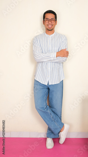 Full body portrait of a man leaning on the wall with arm crossed showing happy face photo