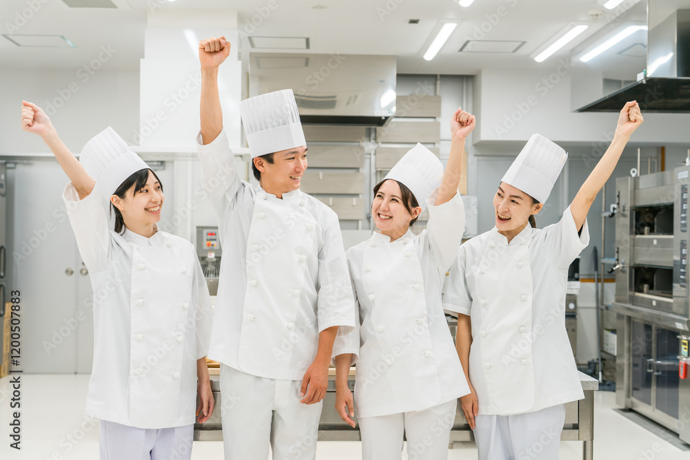 Obraz premium 厨房・キッチンに立つコックコート姿の調理師・シェフ・コックの男女(ガッツポーズ)