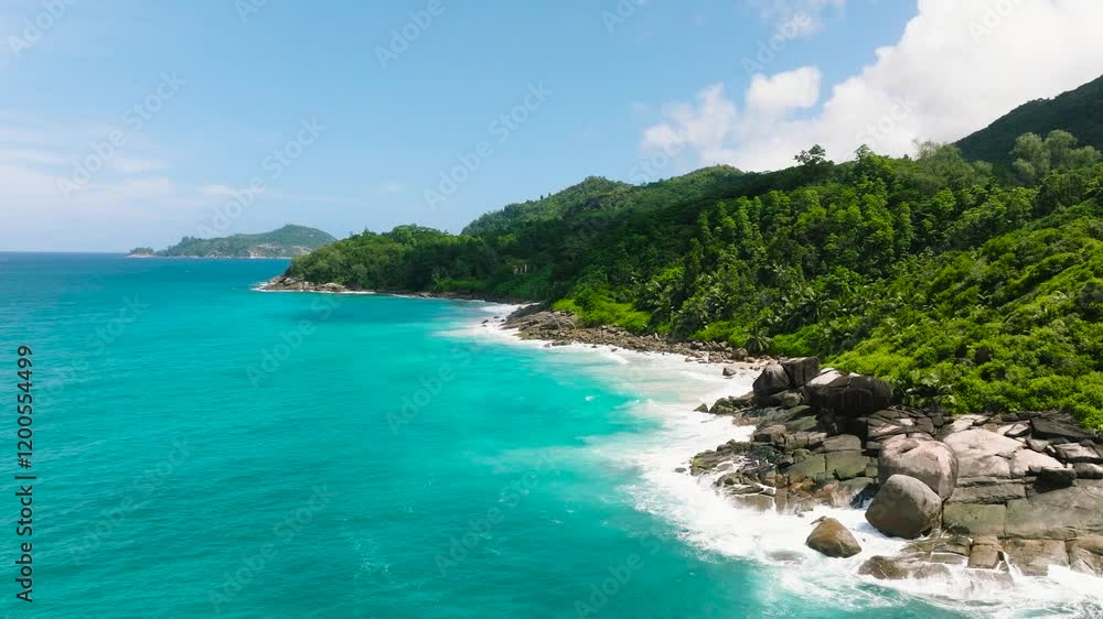 Waves crash against rugged rocks, framed by dense, green tropical vegetation. Seychelles, Mahe. Waves crash against rugged rocks, framed by dense, green tropical vegetation. Seychelles, Mahe.