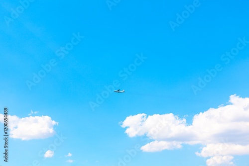 Obraz na płótnie Minimalist photo of a bright blue sky with scattered fluffy white clouds and a small airplane flying in the distance. A serene and open composition perfect for themes of travel, freedom, and adventure w salonie