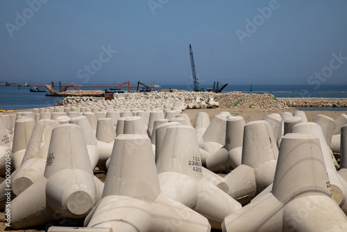 Gangneung-si, Gangwon-do, South Korea - April 13, 2024: Construction site with concrete tetrapods on breakwater against barge and cranes near the sea photo