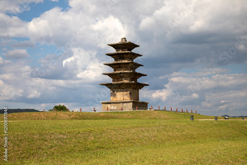 Wangung-ri, Iksan-si, Jeollanam-do, South Korea - May 28, 2024: Low angle view of Five-story Stone Pagoda on grass hill against cloud in the sky photo