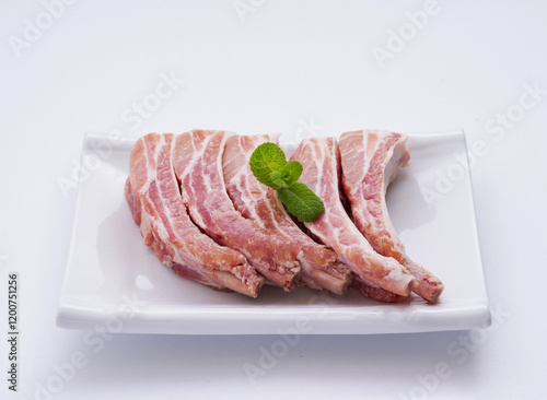 Close up of raw Pork back rib flesh and bone with green herb leaf on rectangular dish and white floor, South Korea photo