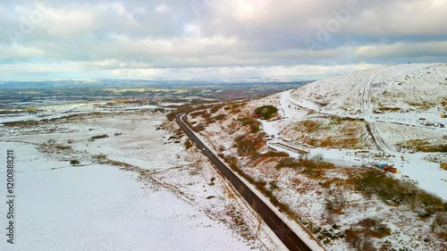 Aerial shot of Cavehill in Belfast, Northern Ireland on a snowy and calm winter day. The camera moves forwards, over the mountain and a road with passing cars. Shot in 4K, 60fps and in Rec709 color. photo