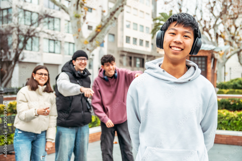 Happy and smiling multiracial group of students having fun together in a university campus, a chinese teenager with headphones is smiling and his friends are pointing at him Happy and smiling multiracial group of students having fun together in a university campus, a chinese teenager with headphones is smiling and his friends are pointing at him
