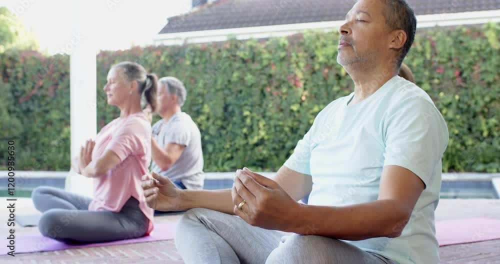 Meditating outdoors, senior friends practicing yoga on mats by pool Meditating outdoors, senior friends practicing yoga on mats by pool