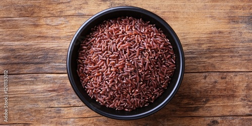 Raw red-skinned Jasmine rice in a black bowl centered on a textured wooden background, highlighting its Asian culinary specialty and natural colors. photo