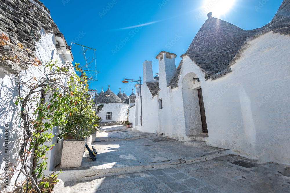 Beautiful stone of Trulli houses with white walls, narrow streets, decorated with flowers, palm trees and other decorations. Spring day, warm with sun and blue skies Selling souvenirs