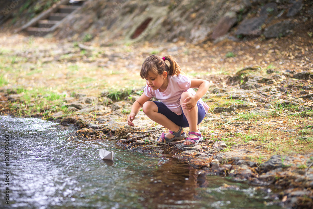 Young girl launching paper boat into stream in nature Young girl launching paper boat into stream in nature