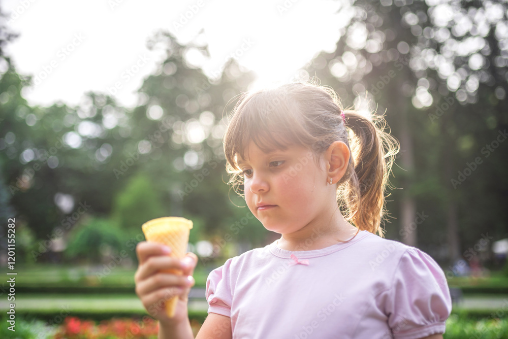 Little girl holding ice cream cone in summer park at sunset Little girl holding ice cream cone in summer park at sunset