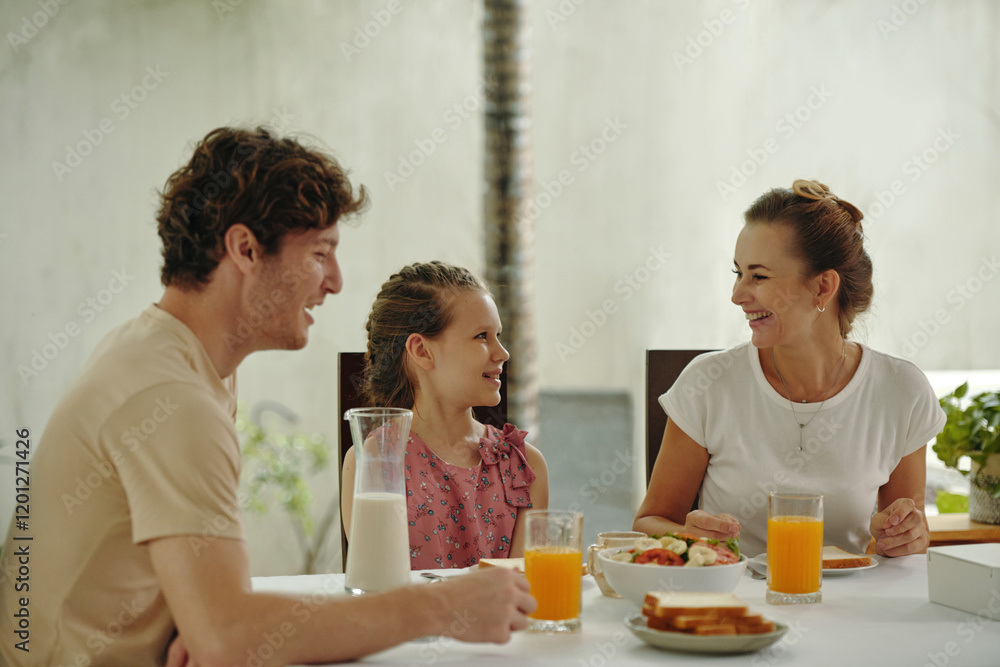 Happy family talking to each other while having breakfast at the table in the room Happy family talking to each other while having breakfast at the table in the room