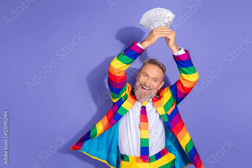 Colorful mature man joyfully brandishes money in rainbow suit against violet backdrop photo