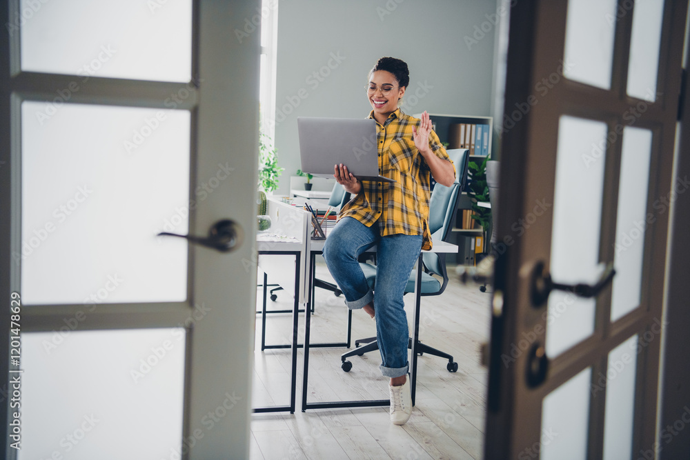 Full size photo of pretty young girl sit table netbook video call talk wear yellow plaid shirt coworking successful nice light office Full size photo of pretty young girl sit table netbook video call talk wear yellow plaid shirt coworking successful nice light office