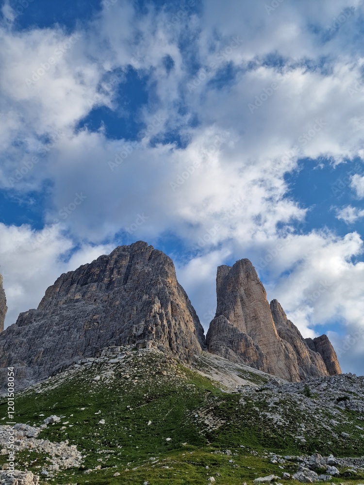 Stunning view of rugged mountain peaks in the Dolomites, sharp, jagged shapes and rocky surfaces, lush green grass, fluffy clouds, hiking path to Tre Cime di Lavaredo Stunning view of rugged mountain peaks in the Dolomites, sharp, jagged shapes and rocky surfaces, lush green grass, fluffy clouds, hiking path to Tre Cime di Lavaredo